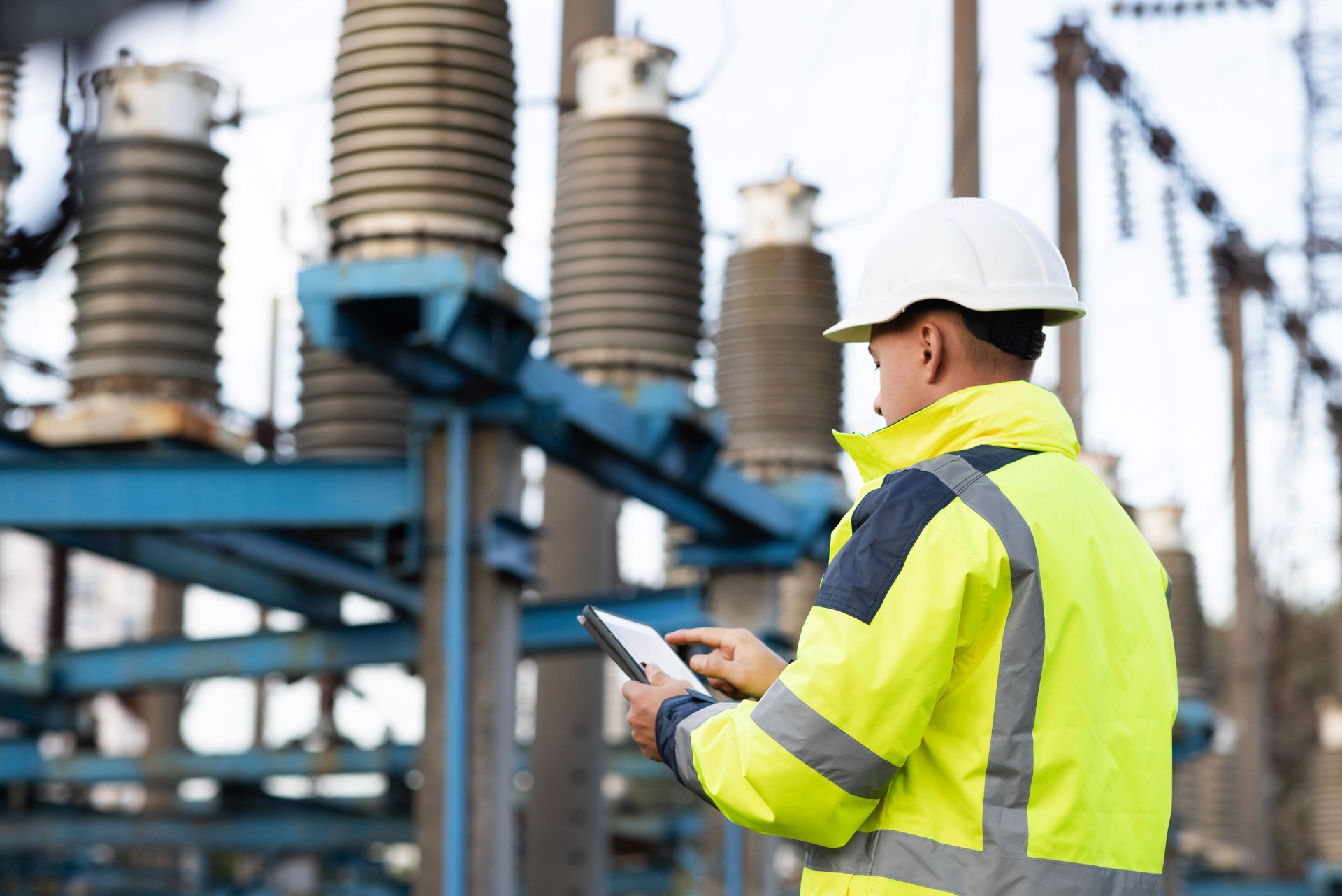 Electrical engineer studying reading on tablet. Electrical worker engineer a working with digital tablet, power near tower with electricity. Energy business technology industry concept